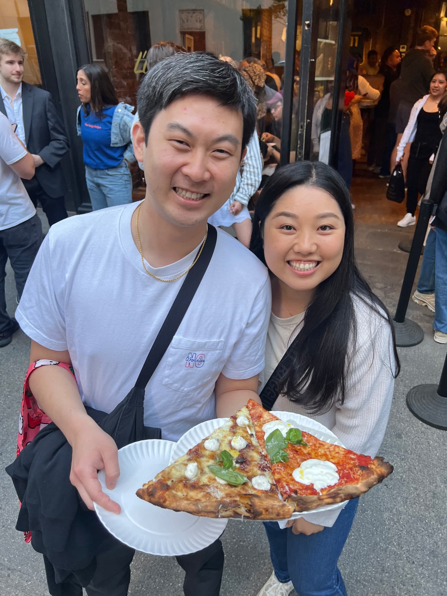 Guide and his fiancée holding two slices of pizza on a busy street